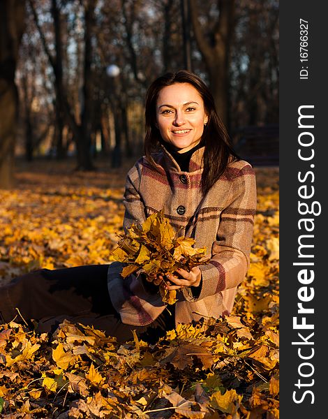 Beautiful young woman sitting in autumn leaves