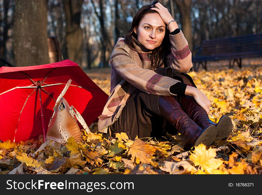 Beautiful young woman sitting in autumn leaves