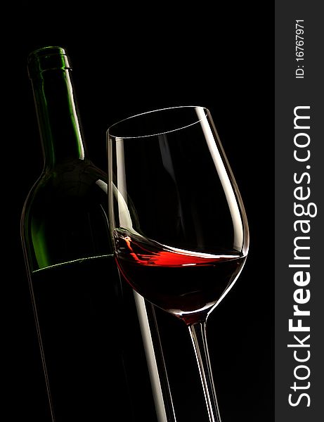 Glass of red wine with a bottle and black background