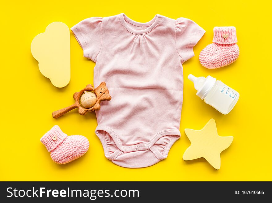 Pink bodysuit for baby girl near children`s things on yellow background top-down