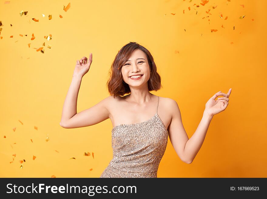Young woman dancing under confetti at home, celebrating birthday.