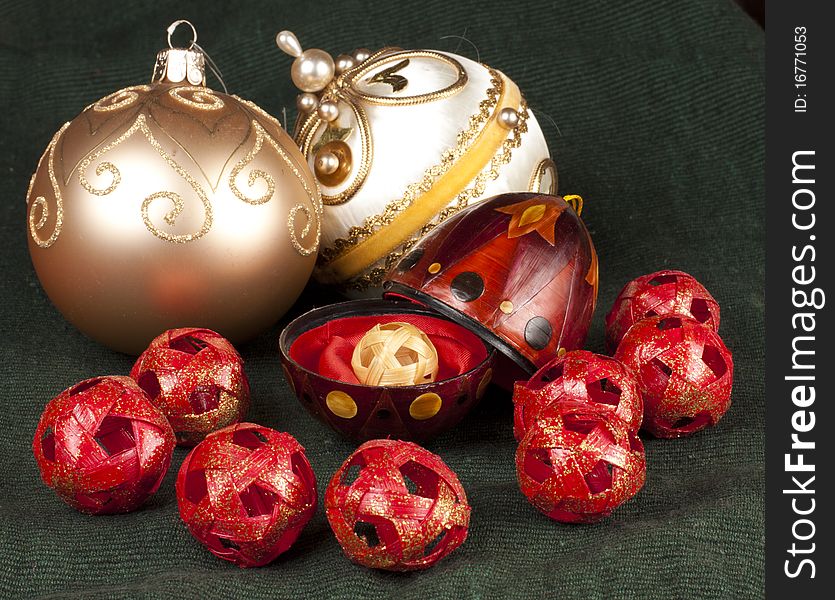 An open red ornament on a green background with gold baubles all around with a gold ball inside. An open red ornament on a green background with gold baubles all around with a gold ball inside