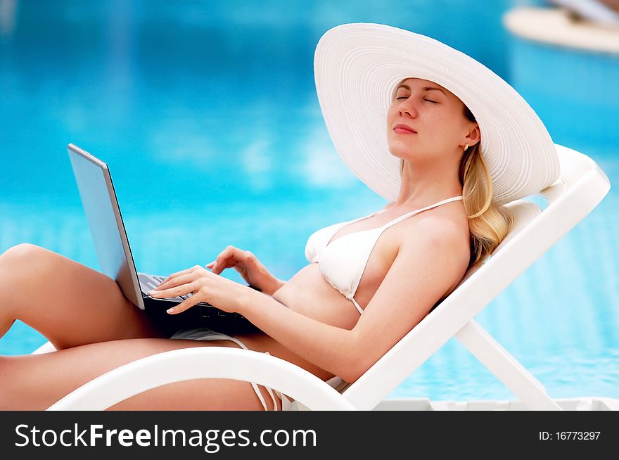 Young women relaxing near waterpool with laptop.