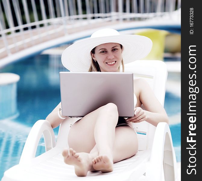 Young women relaxing near waterpool with laptop.