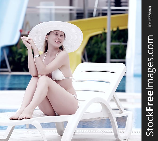 Young women in white bikini and white hat relaxing near waterpool
