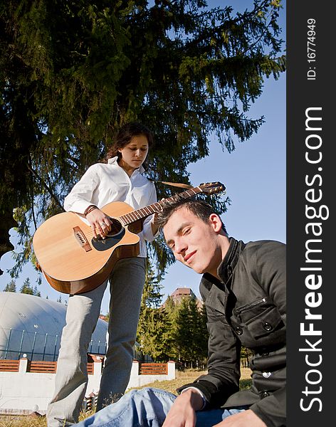 Happy couple playing guitar on the middle of nature, under a tree