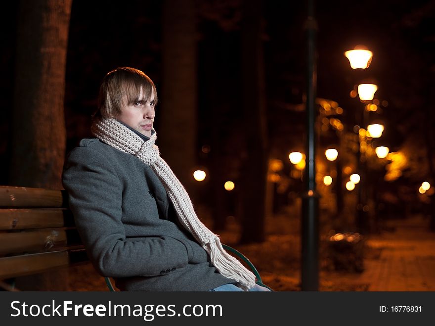 Young man in coat sitting at night park alley. Young man in coat sitting at night park alley