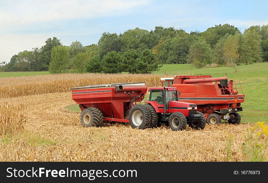 Red combine and tractor with a wagon harvesting corn