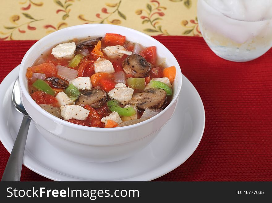 Chicken vegetable soup with mushrooms, tomatoes, peppers and onions in a white bowl