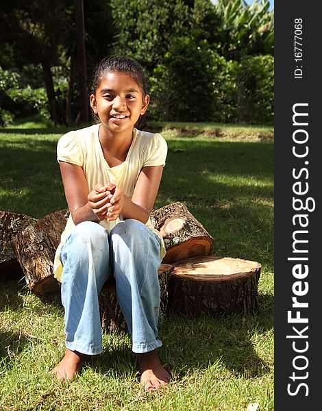 Young bare footed school girl sitting on cut logs in the bright sunshine. Young bare footed school girl sitting on cut logs in the bright sunshine
