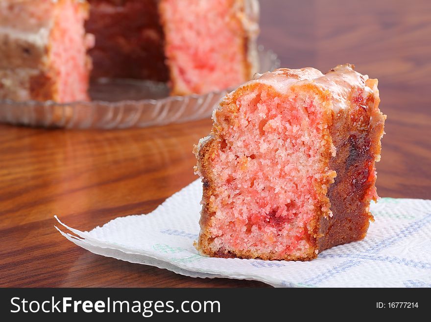 Slice of strawberry cake on a napkin with whole cake in background