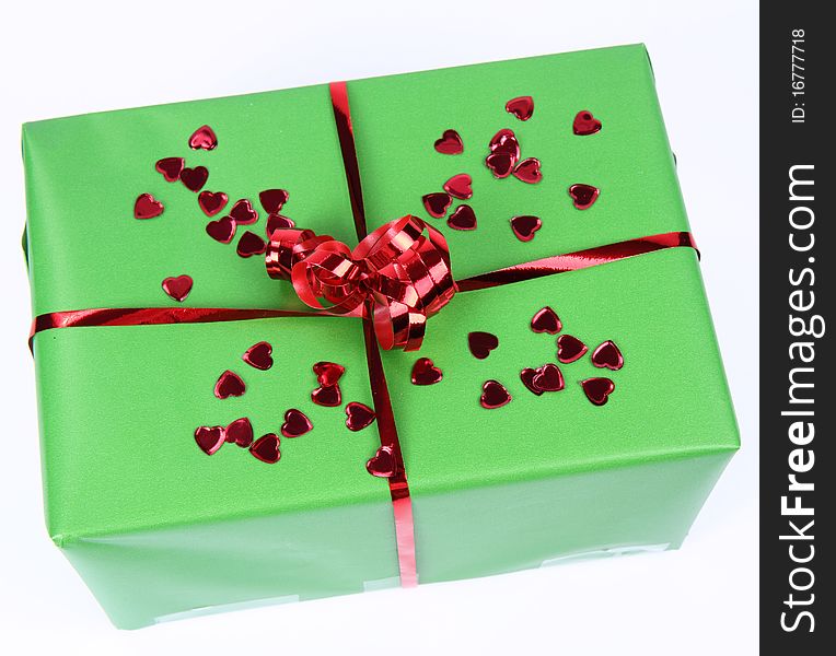 Gift in green wrapping with a red bow decorated with heart shaped confetti