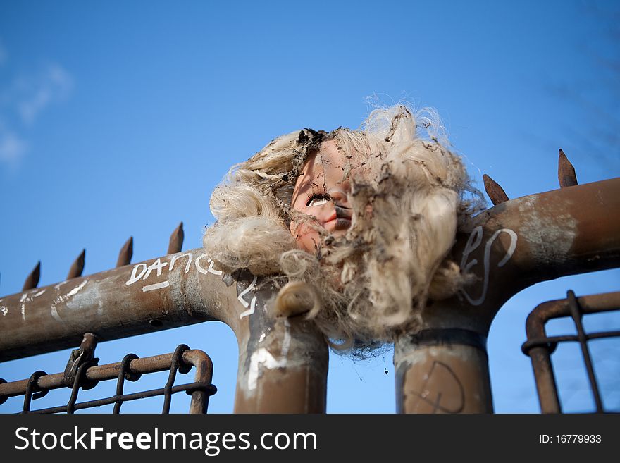A burned doll head is pierced by a rusty metal fence. A burned doll head is pierced by a rusty metal fence.