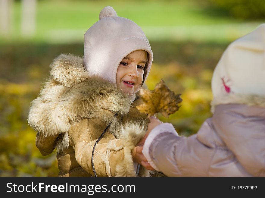 Two little girls playing with autumn leave in the park