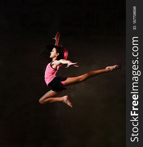 Young slim athletic girl gymnast dancer jumping up flying with her arm up stretching doing gymnastic exercises in studio