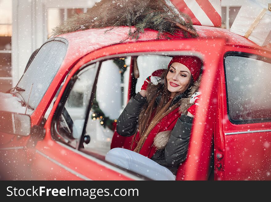 Pleasant fashionable winter girl smiling posing at red vintage car surrounded by snowflakes