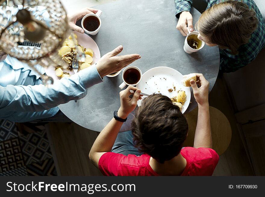 Family breakfast at the oval table by the window. Father and two sons eating potatoes and drinking coffee from white ceramic mugs. Top view through a crystal chandelier. Weekend Family Customs Concept