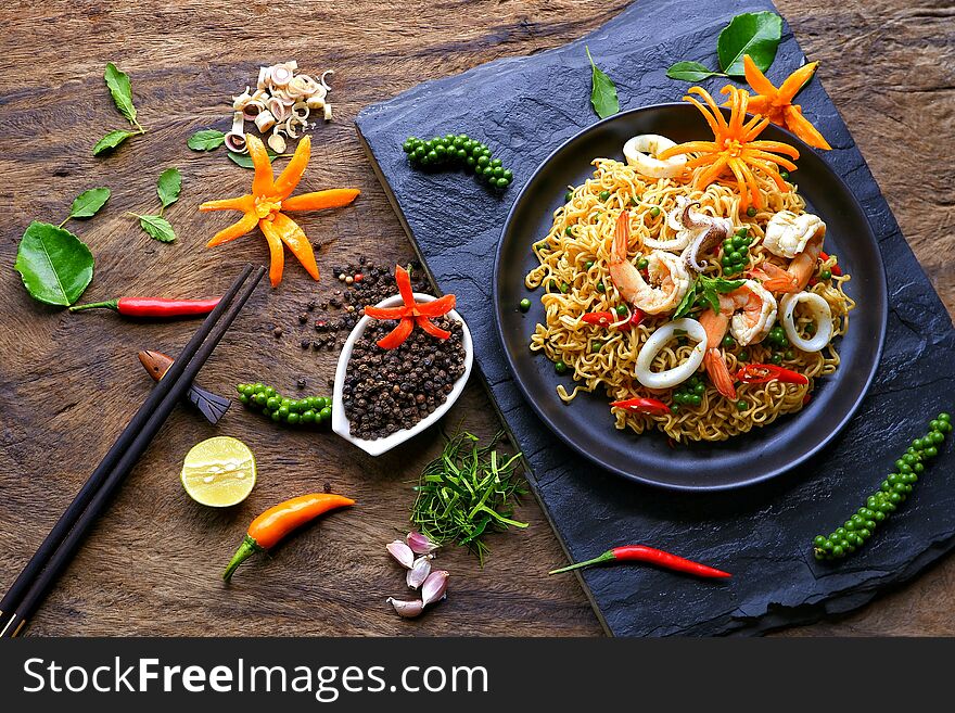 instant noodles with stir fried spicy seafood and various herbs on black stone plate