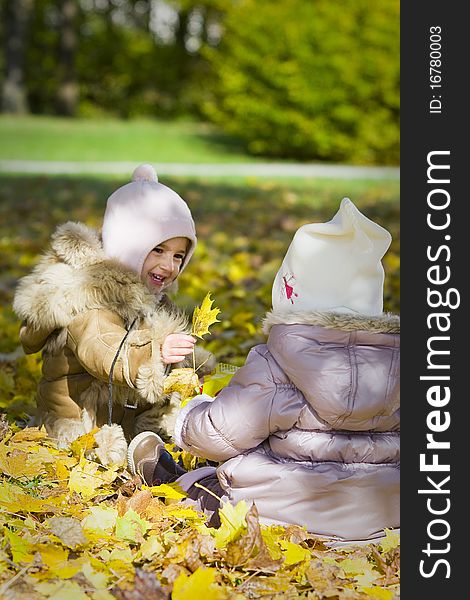 Two little girls playing with autumn leave in the park