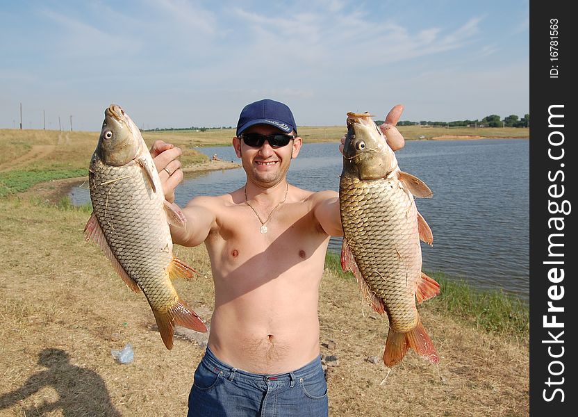 A fisherman with two big carp on the background of the lake. A fisherman with two big carp on the background of the lake