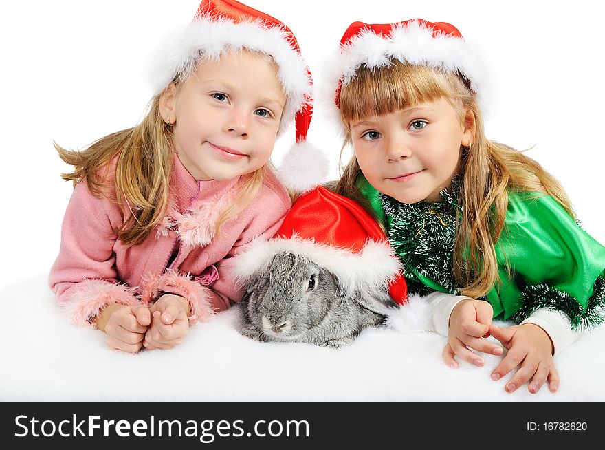 Two smiling girls with a rabbit in caps of Santy. Two smiling girls with a rabbit in caps of Santy