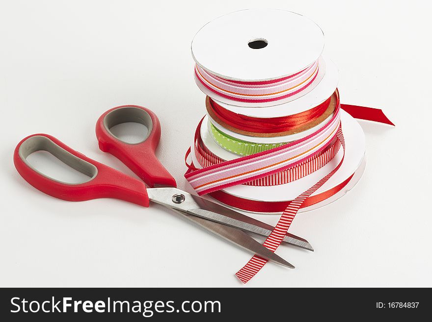 Five spools of red and green ribbon with scissors on a white table. Five spools of red and green ribbon with scissors on a white table