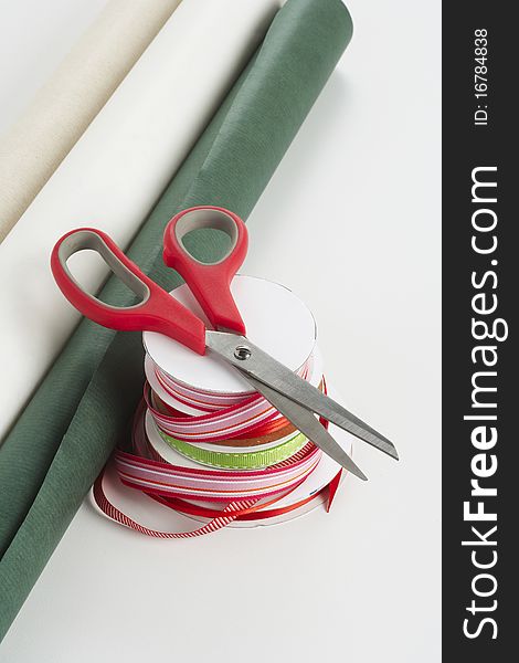 Red handled scissors on top of a stack of red and green ribbon with gift wrapping paper. Red handled scissors on top of a stack of red and green ribbon with gift wrapping paper