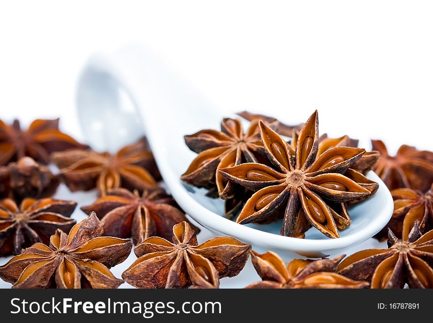 Star Anise scattered on the ground and in white ceramic spoon, isolated on white studio background