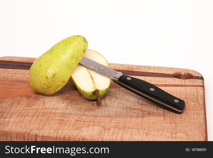 A Single Pear on a Wood Cutting Board with Black Knife Isolated against a White Background. A Single Pear on a Wood Cutting Board with Black Knife Isolated against a White Background