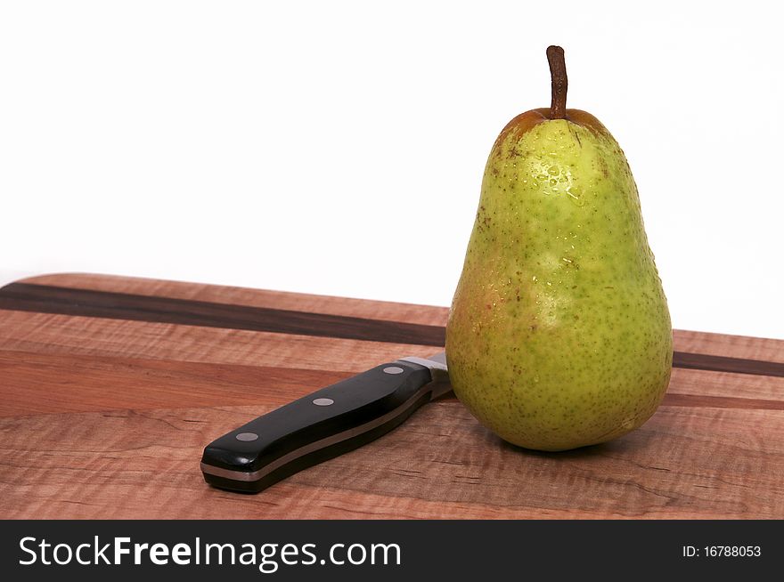A Single Pear on a Wood Cutting Board with Black Knife Isolated against a White Background