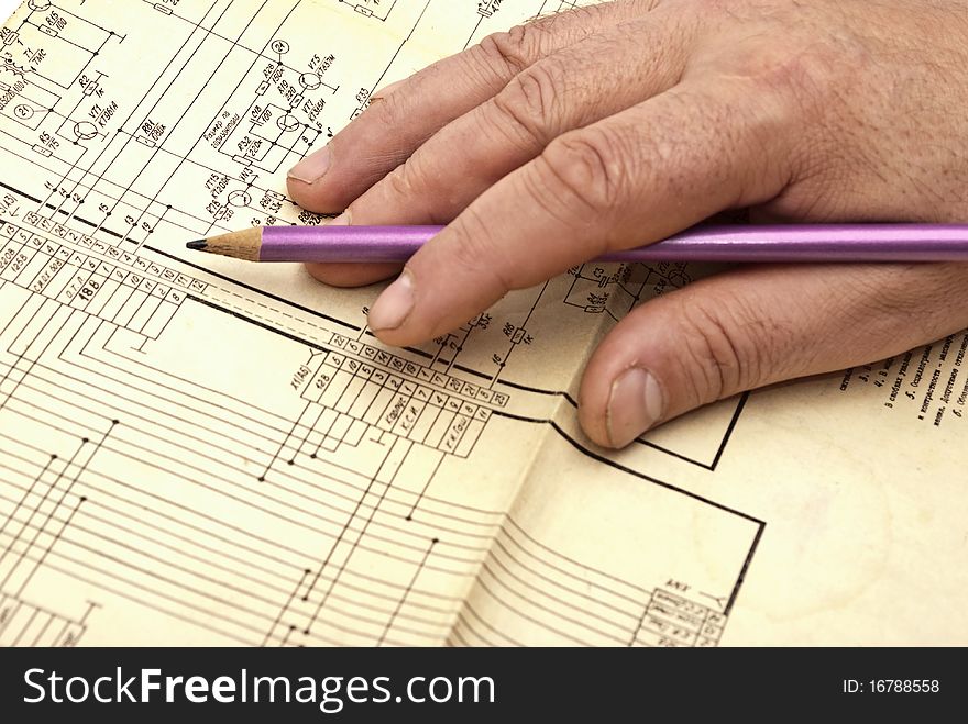 Human hand with pencil on electroscheme in operation