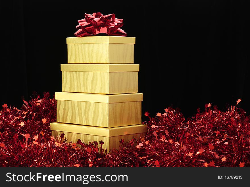 Four gold boxes stacked with a red bow on top one and sitting on red tinsel garland. Four gold boxes stacked with a red bow on top one and sitting on red tinsel garland