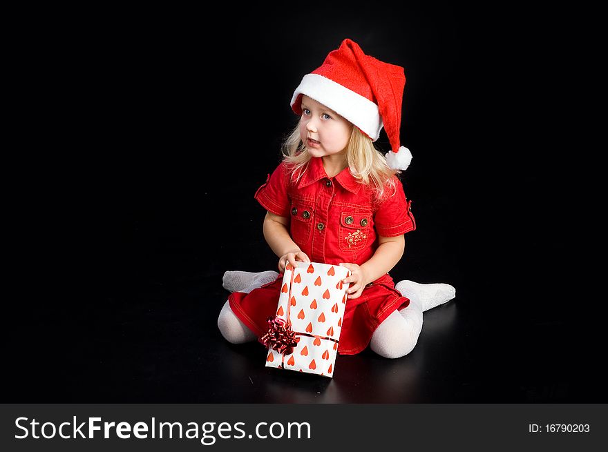 Surprised girl in red dress and santa cap with gift box. Isolated on black. Surprised girl in red dress and santa cap with gift box. Isolated on black