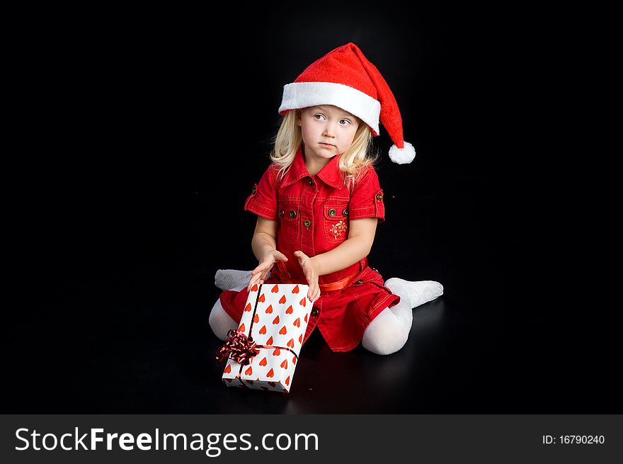 Surprised girl in red dress and santa cap with gift box. Isolated on black. Surprised girl in red dress and santa cap with gift box. Isolated on black