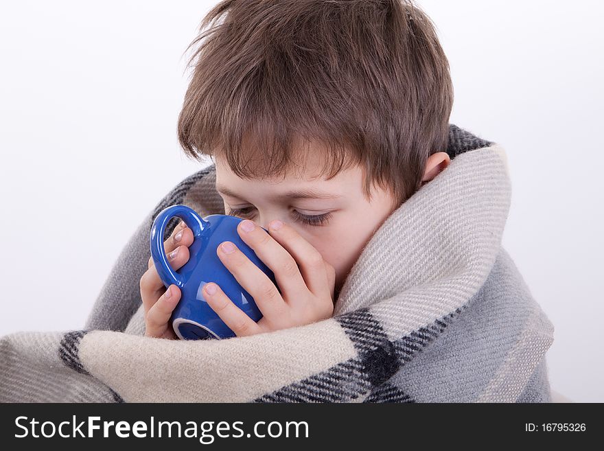 The boy covered by a checkered plaid, drinks from a dark blue cup