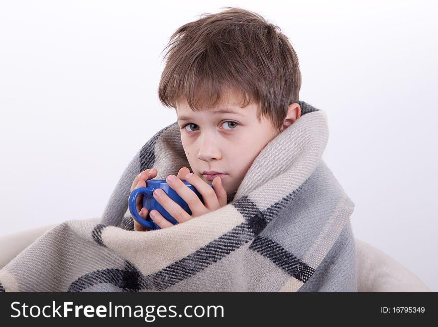 The boy covered by a checkered plaid, drinks from a dark blue cup