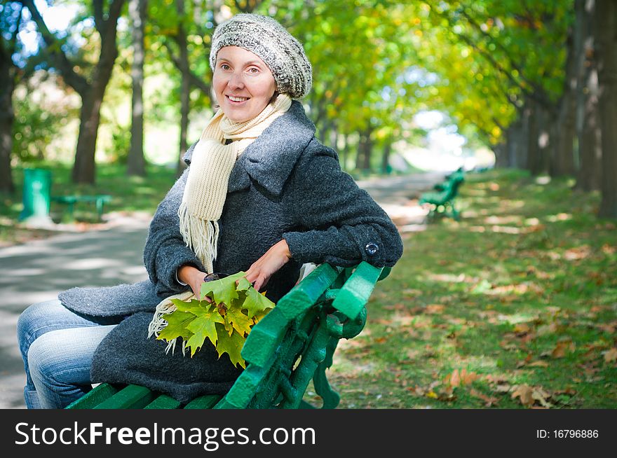 Pretty young woman resting on a bench in autumn park