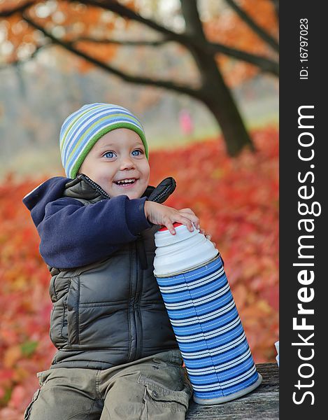 Little cute boy drinks tea from a thermos in the autumn park