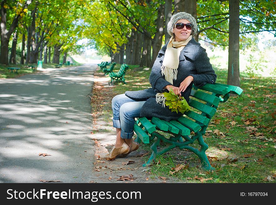 Pretty young woman resting on a bench in autumn park