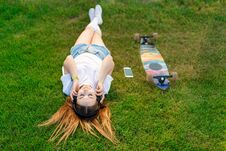 Young Girl Enjoy Lay In Green Lawn And Listening Music After Riding On Her Logboard Royalty Free Stock Images