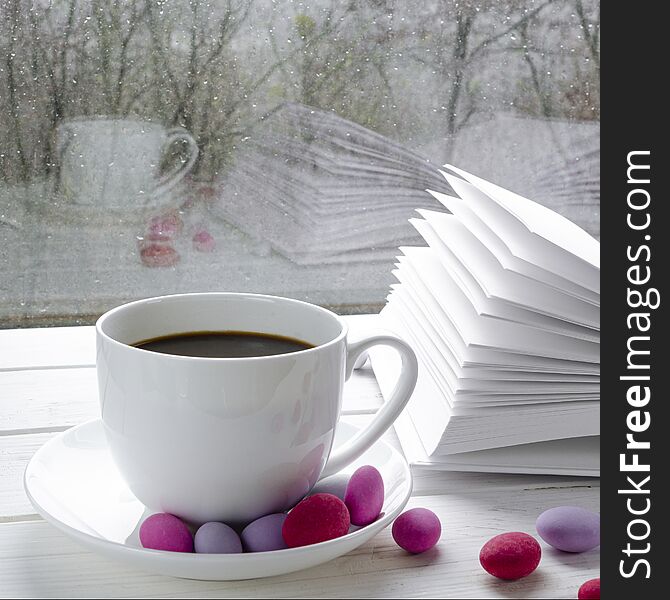 Cozy concept: a white cup of coffee stands on a white wooden table next to a white open book and colorful candy against the