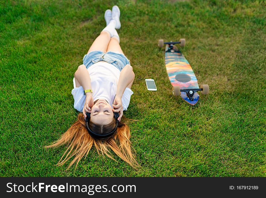 Young girl enjoy lay in green lawn and listening music after riding on her logboard