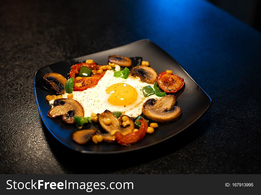 Freshly fried scrambled eggs with vegetables on a black plate.