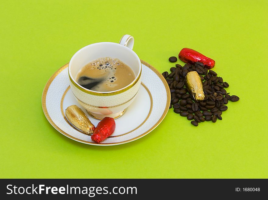 Coffee cup on green background, chocolates and coffeebeans. Coffee cup on green background, chocolates and coffeebeans