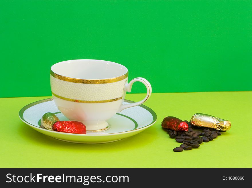 Coffee cup on green background, chocolates and coffeebeans. Coffee cup on green background, chocolates and coffeebeans