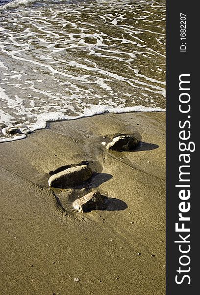 Brown sandy beach with three stones washed ove by retreating sea water. Brown sandy beach with three stones washed ove by retreating sea water