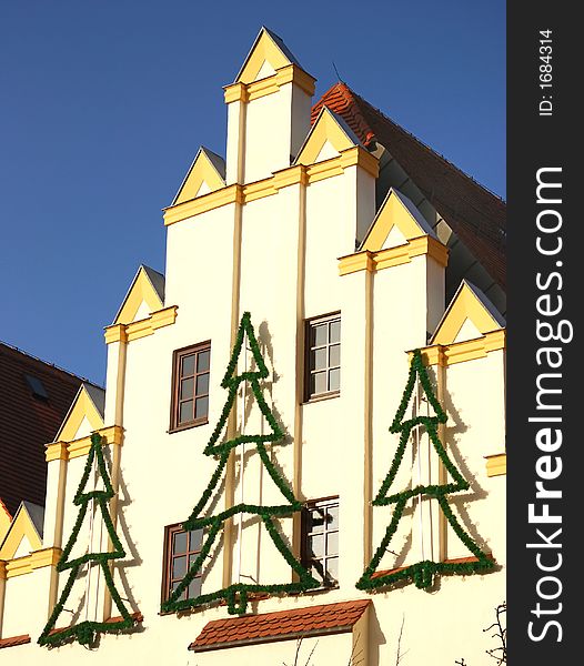 The image shows a house facade with christmas decoration. Some tree figures made of fir branches are fixed at the wall. The picture was shot at a sunny day with deep blue sky. The image shows a house facade with christmas decoration. Some tree figures made of fir branches are fixed at the wall. The picture was shot at a sunny day with deep blue sky.