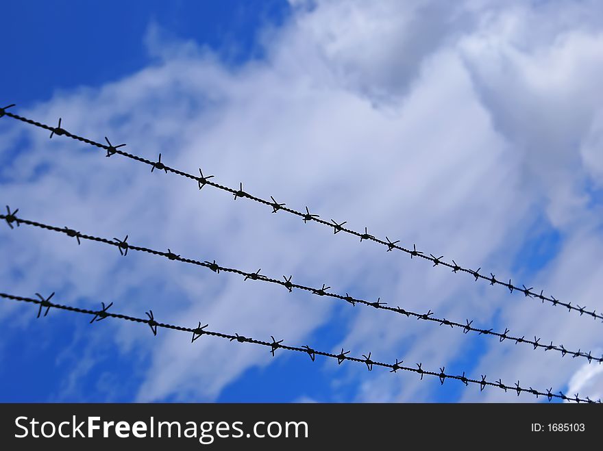 Long barbed wire 3 rows over cloudy sky