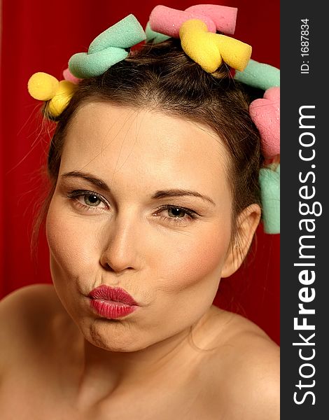 Close up of young woman with colourful curlers in her hair and red lips