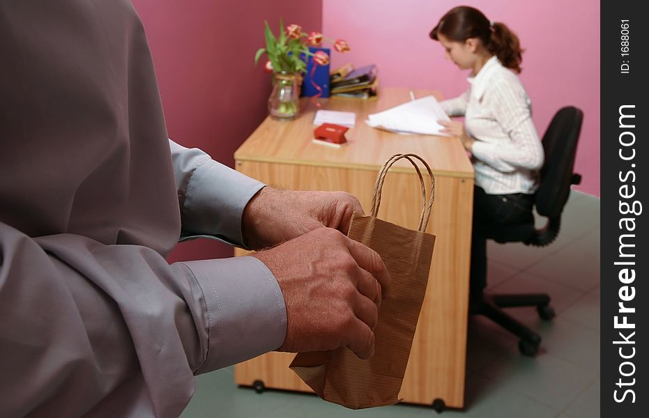 Work environment- man bringing some gift for a woman working in a background